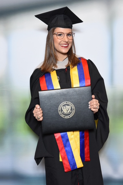Sonia at her SCAD graduation holding her MFA diploma, wearing a Venezuelan flag stole
